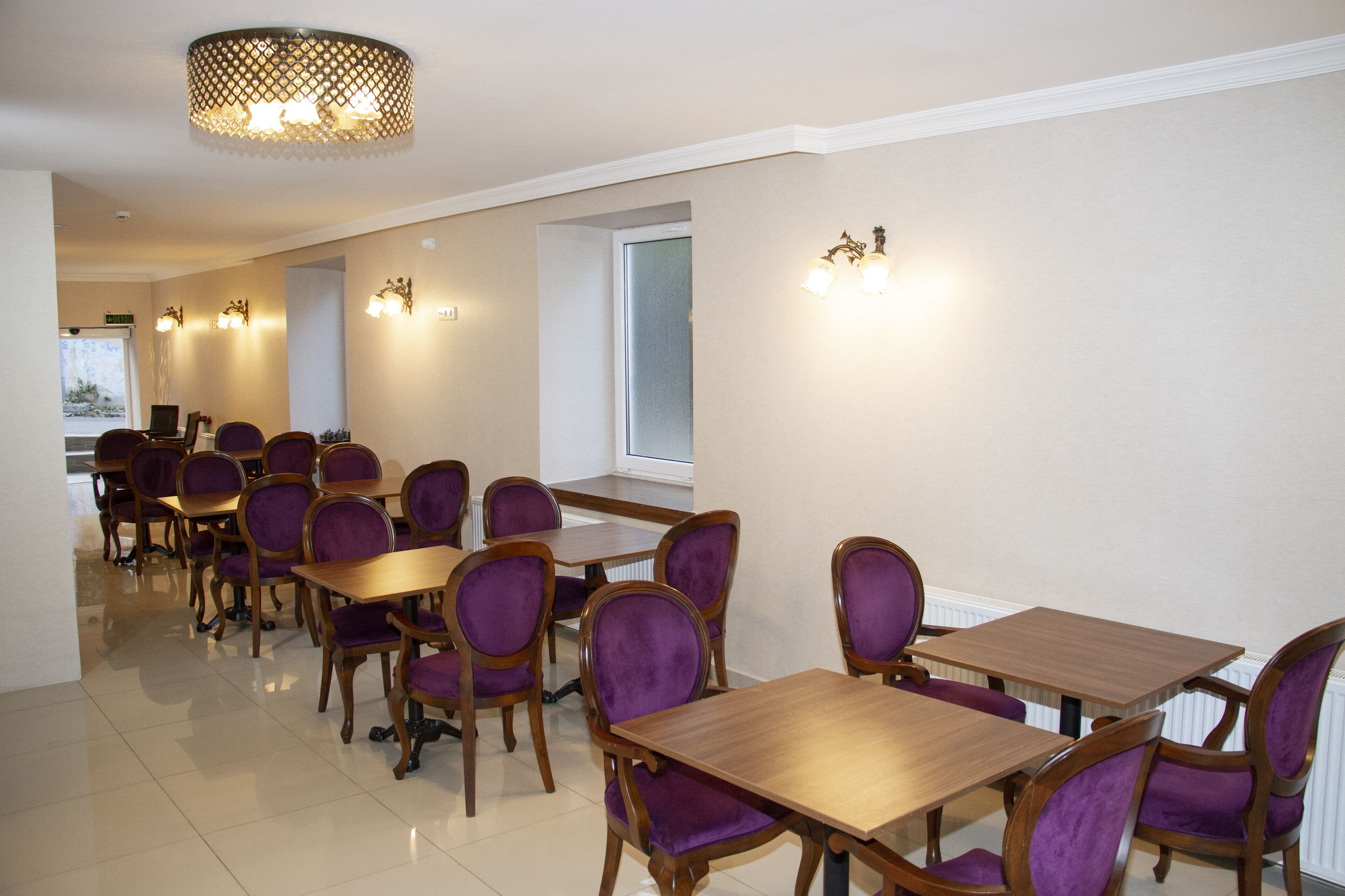 Un espace repas avec des tables en bois et des chaises à revêtement violet, un lustre et des appliques murales.