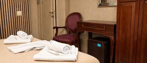 A hotel room with a bed, a desk, a chair, a wardrobe, and a small refrigerator.