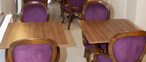 A dining area with wooden tables and purple upholstered chairs, arranged in rows.
