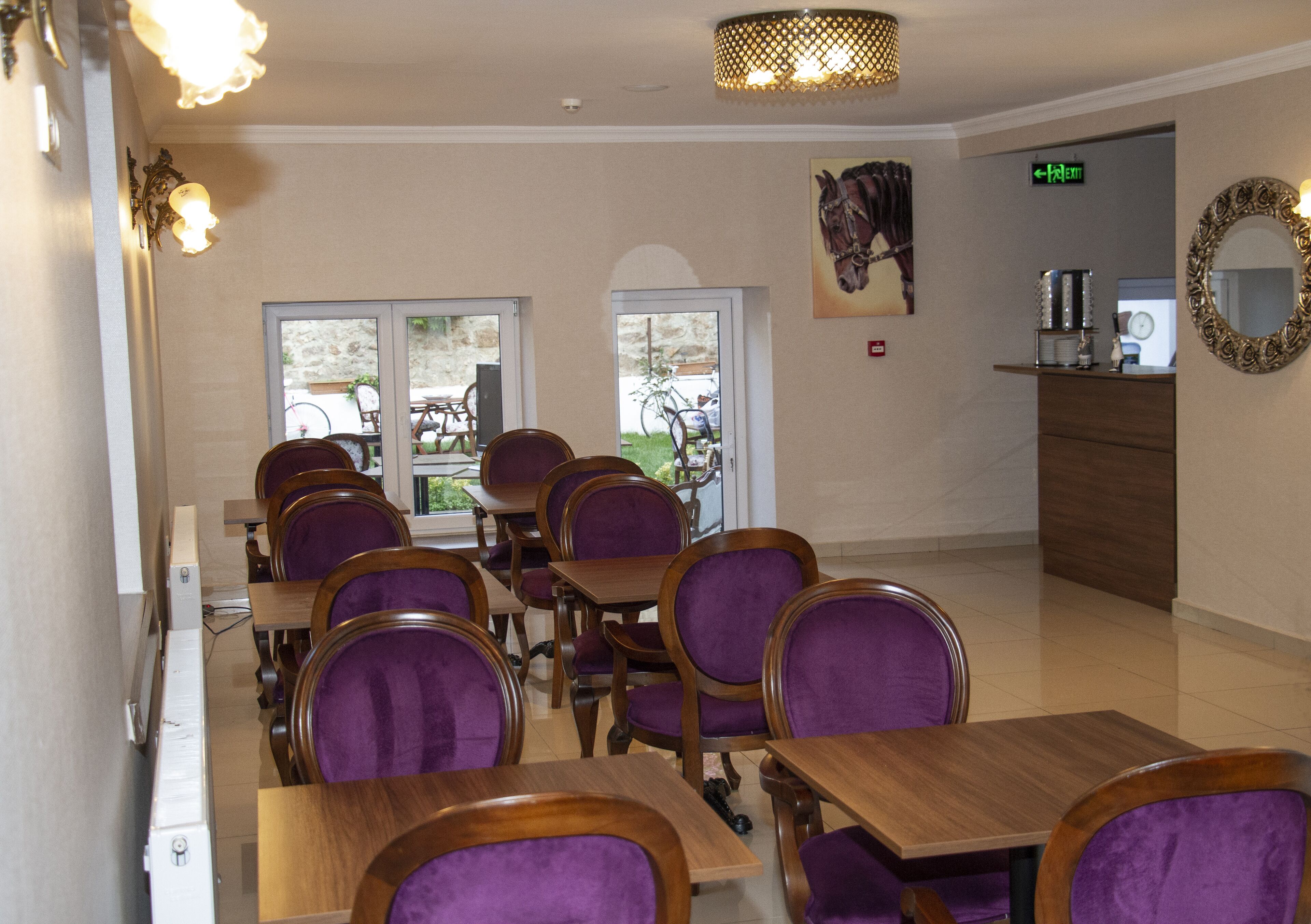 Un comedor con mesas de madera y sillas tapizadas en color morado, un espejo en la pared y una puerta que da al exterior.