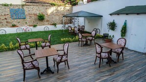 An outdoor patio with wooden tables and chairs, a covered seating area, and a stone wall with a decorative blue pattern. - Pelit Boutique Hotel (Adalar)