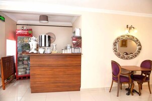 Un área de recepción con mostrador de madera, un refrigerador de Coca-Cola, una máquina de café y un espejo en la pared.