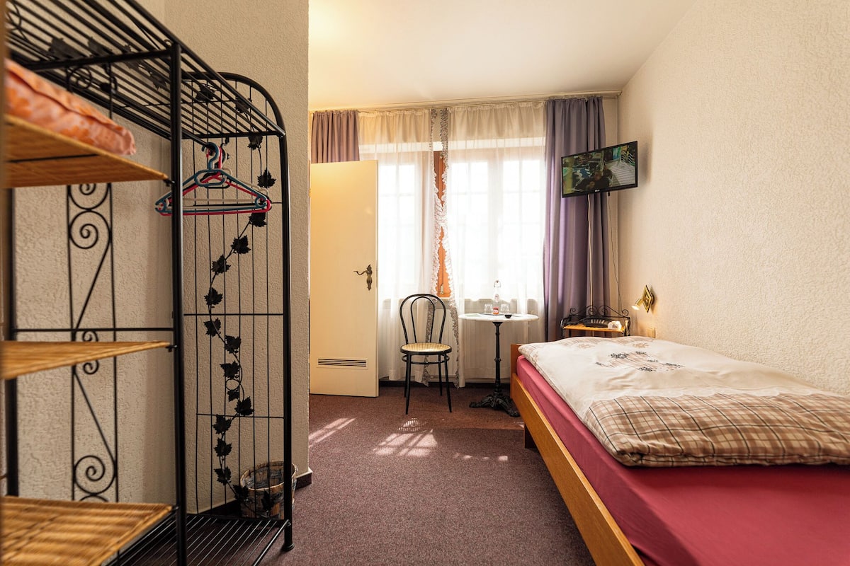 A room with a bunk bed, a desk, a chair, and a TV mounted on the wall.