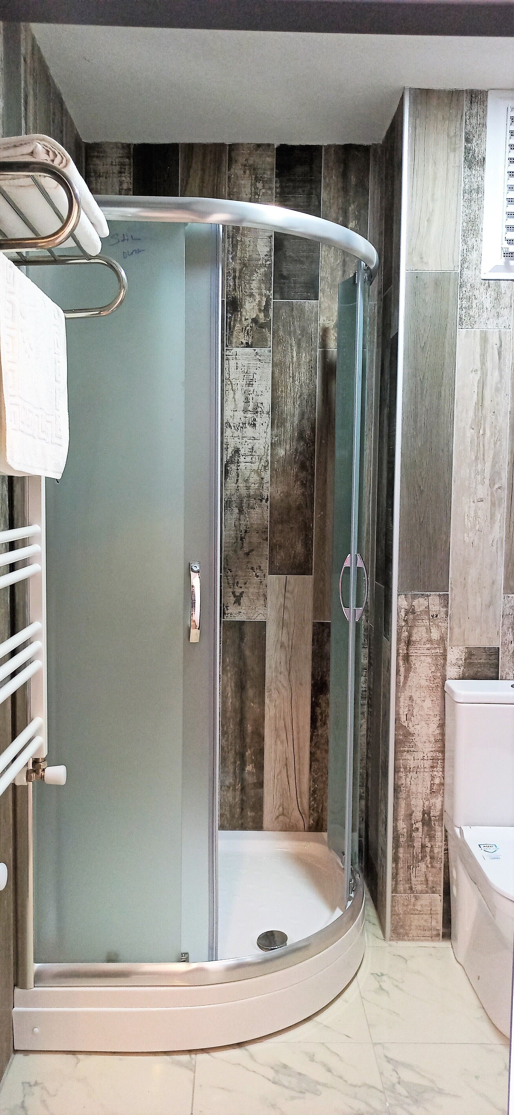 Un baño moderno con ducha de vidrio, inodoro blanco y piso de mármol.