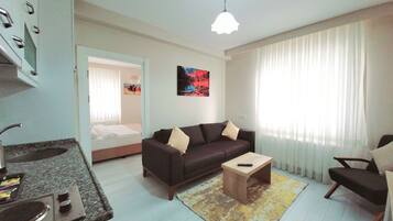 A modern living room with a sofa, coffee table, and a small kitchen area with a sink and stove.