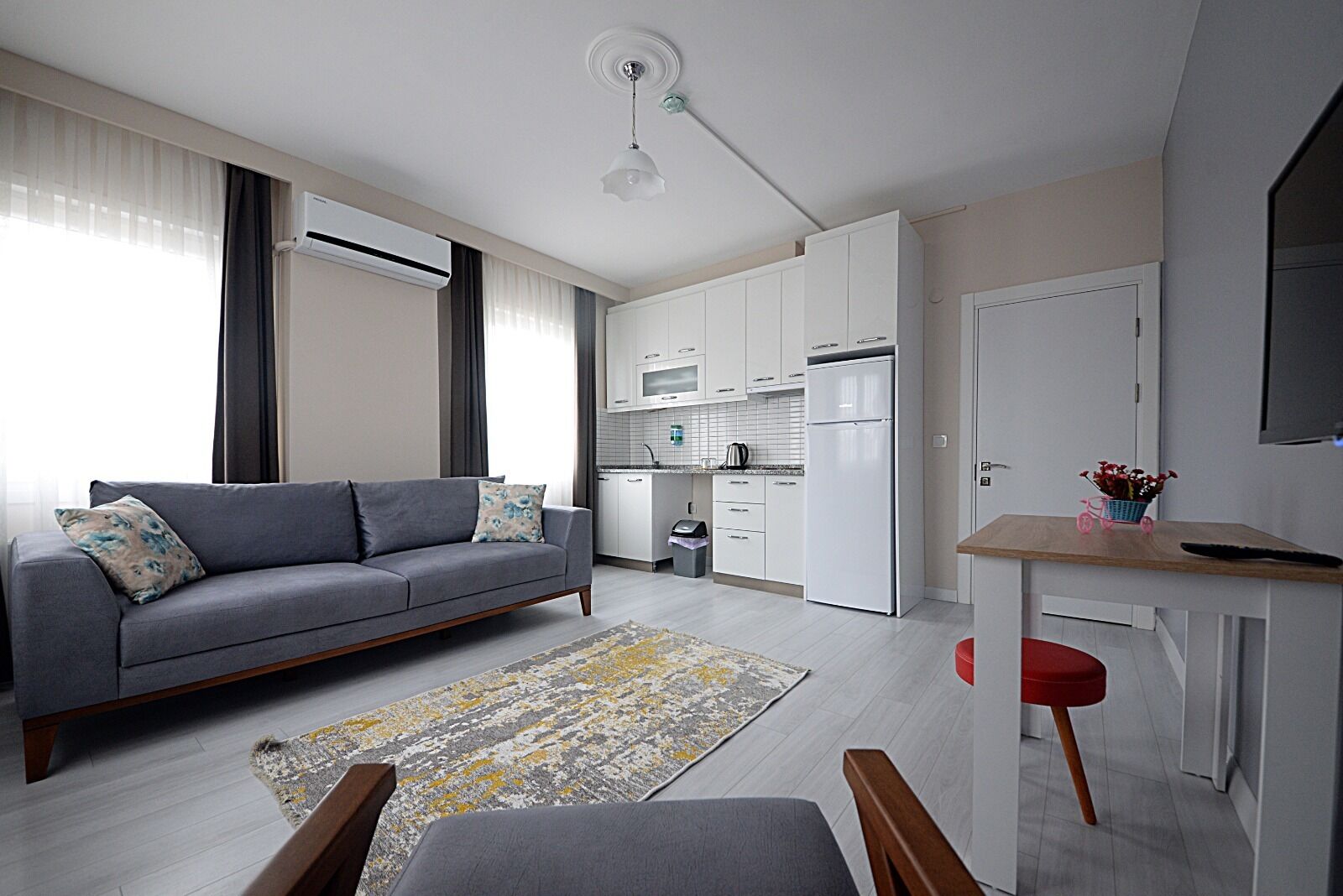 A modern apartment with a grey sofa, a small dining table, a kitchen area, and a living room.