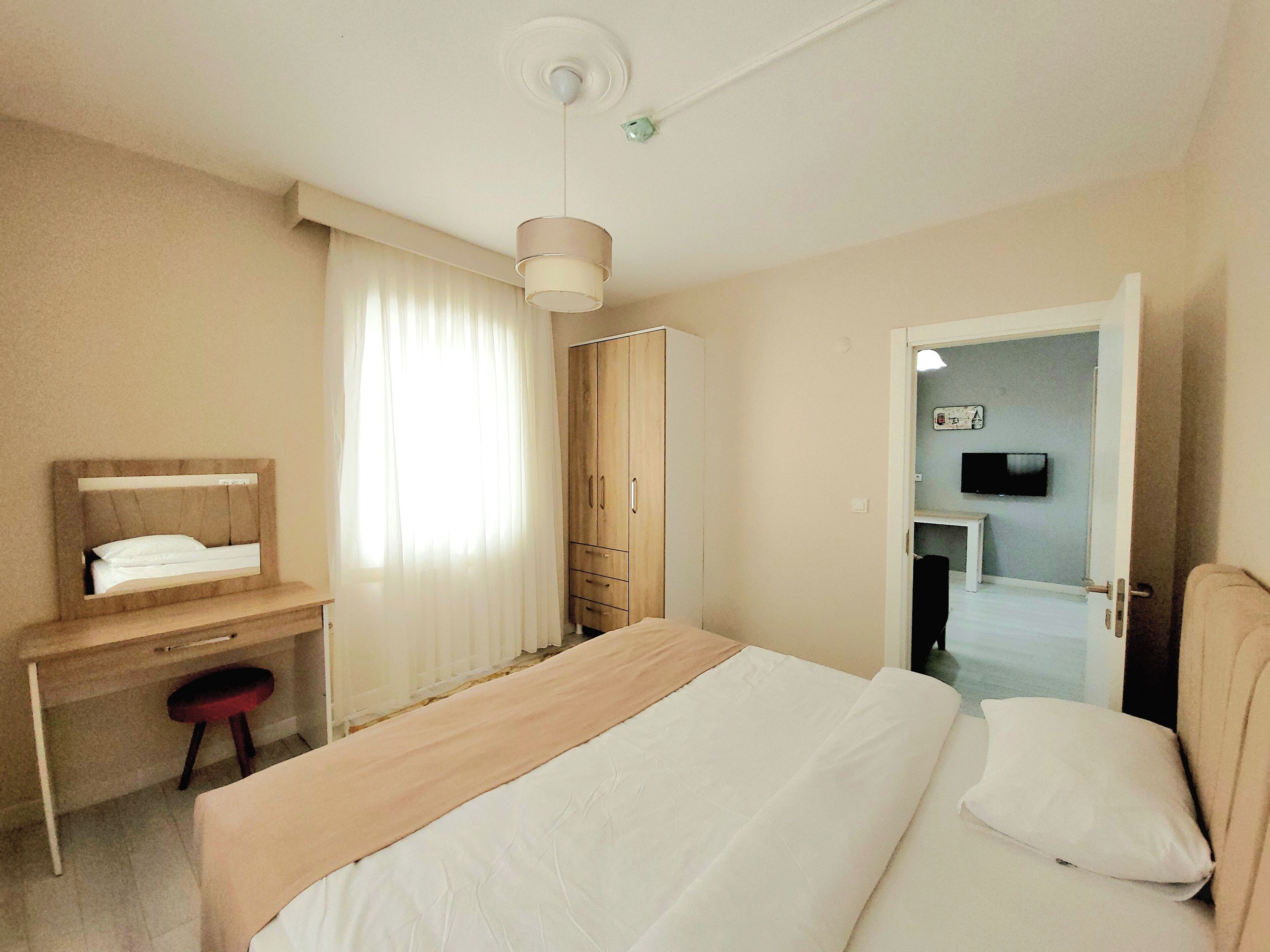 A hotel room with a bed, a desk, a chair, a wardrobe, and a television.