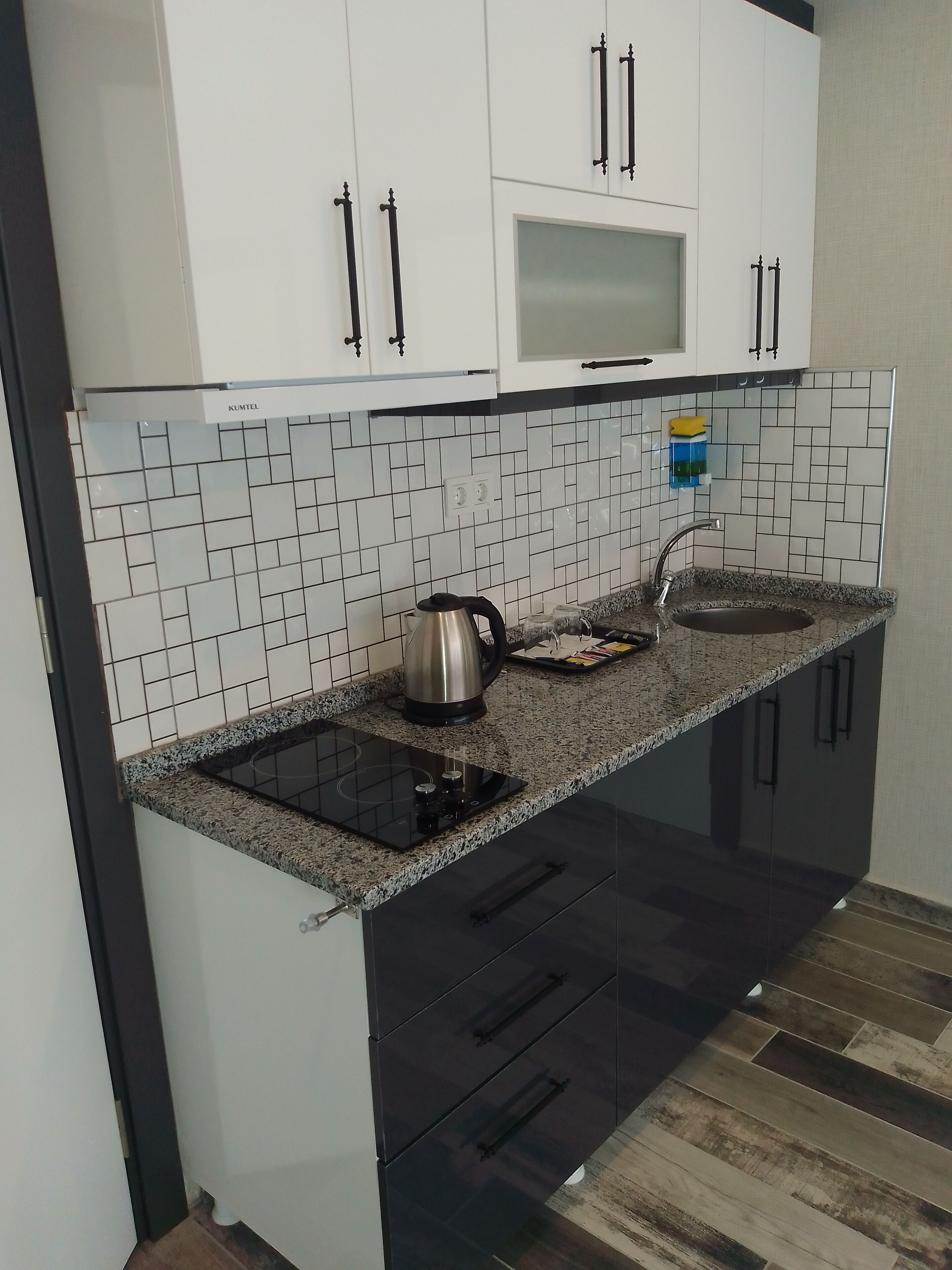 A modern kitchen with white cabinets, a black countertop, and a stainless steel kettle.