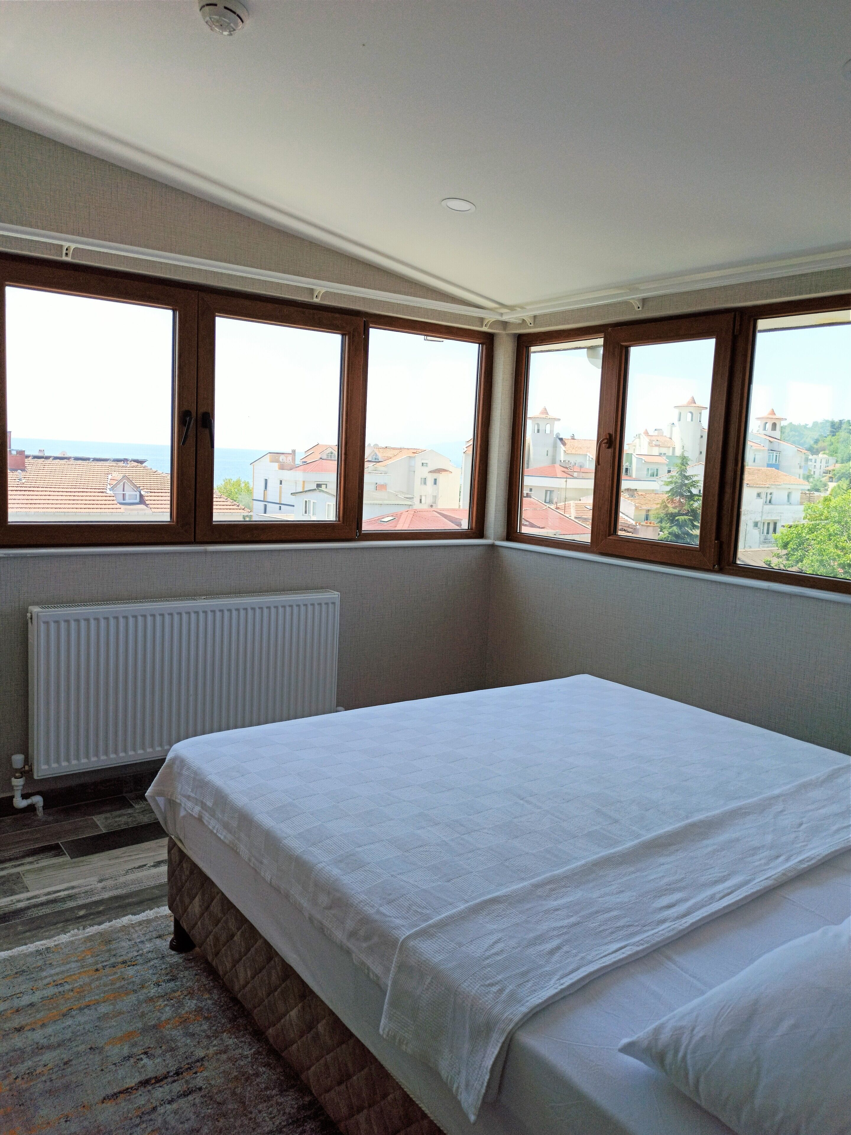A bedroom with a bed, a radiator, and large windows with a city view.