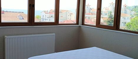 A bedroom with a bed, a radiator, and large windows with a city view.