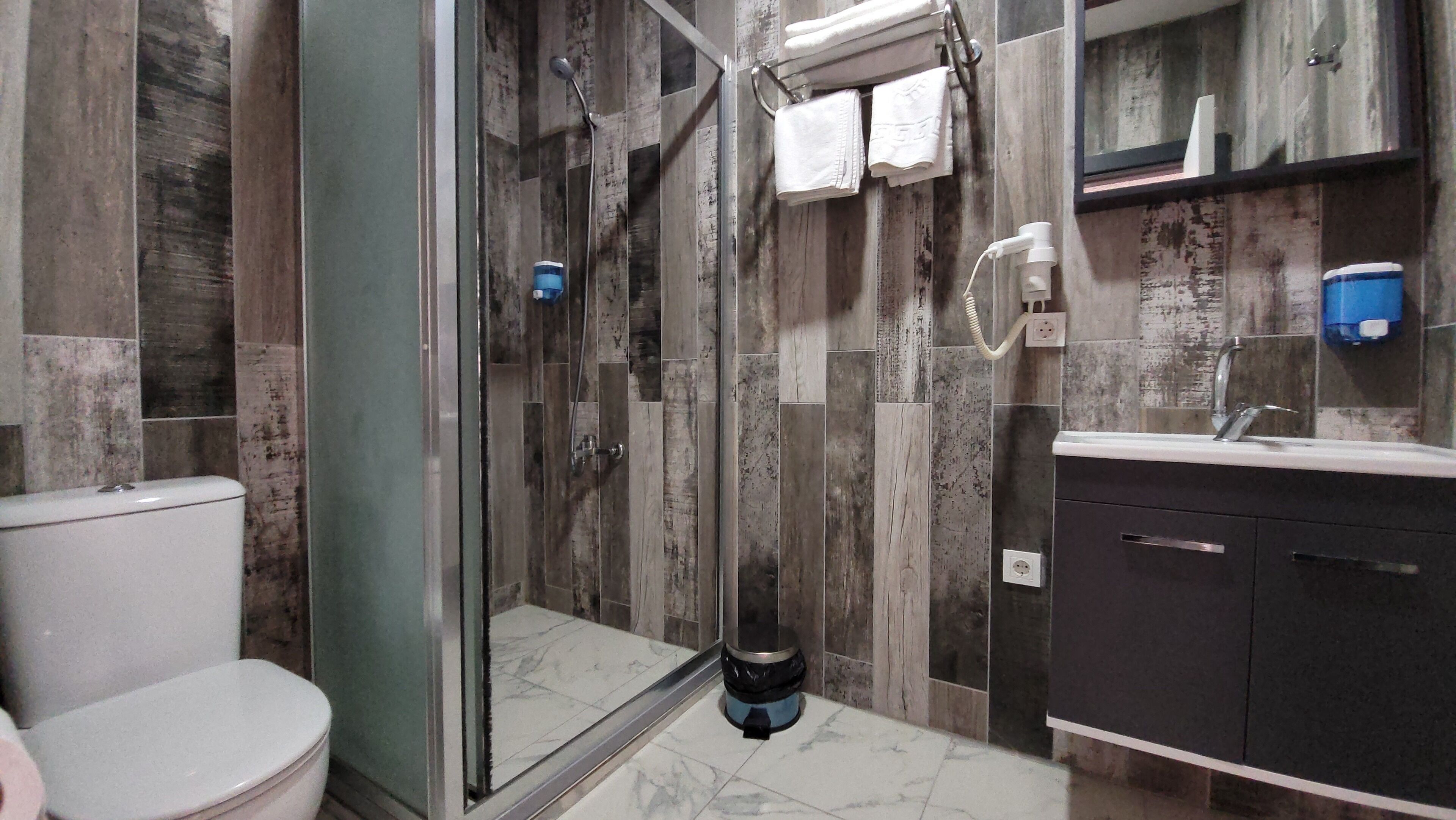 A modern bathroom with a glass-enclosed shower, a toilet, and a sink with a dark cabinet.