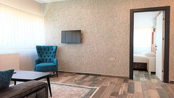 A room with a patterned wall, a blue armchair, a small table, and a bed with a patterned headboard.