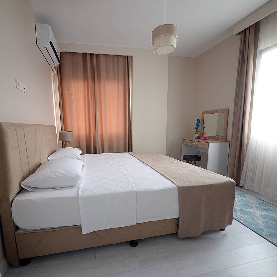 A hotel room with a bed, a desk, a chair, an air conditioning unit, a lamp, and a window with curtains.