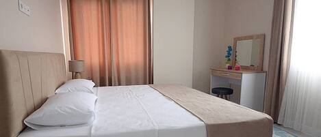 A hotel room with a bed, a desk, a chair, an air conditioning unit, a lamp, and a window with curtains.