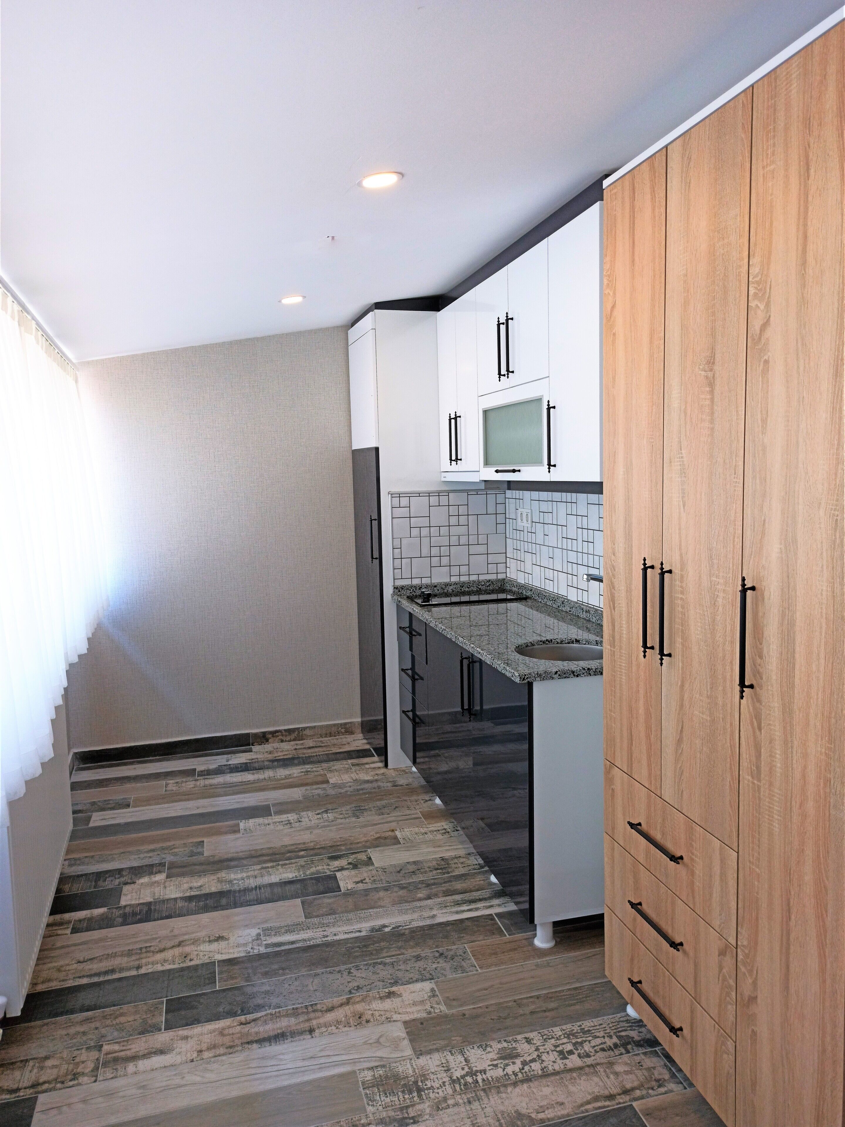 Una cocina moderna con armarios blancos, un mueble de madera, salpicadero de azulejos y microondas integrado.
