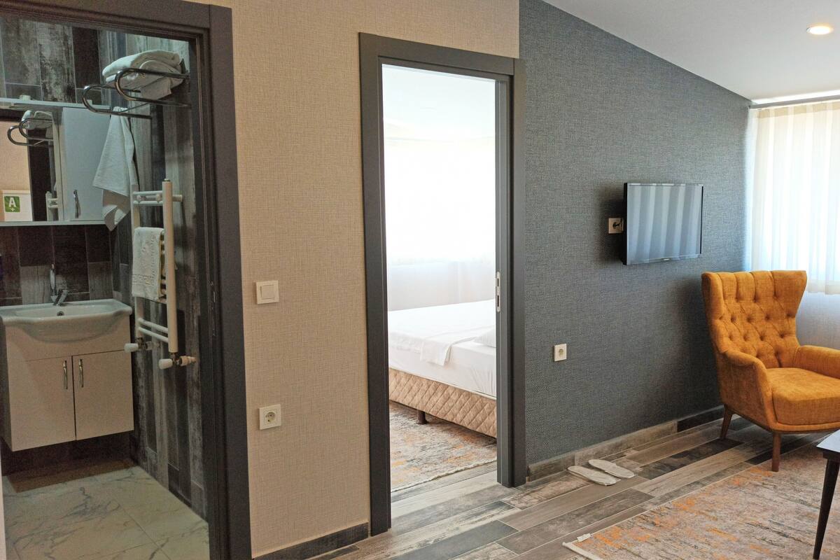 A hotel room with a bathroom, a bed, a TV, a chair, and a small table.
