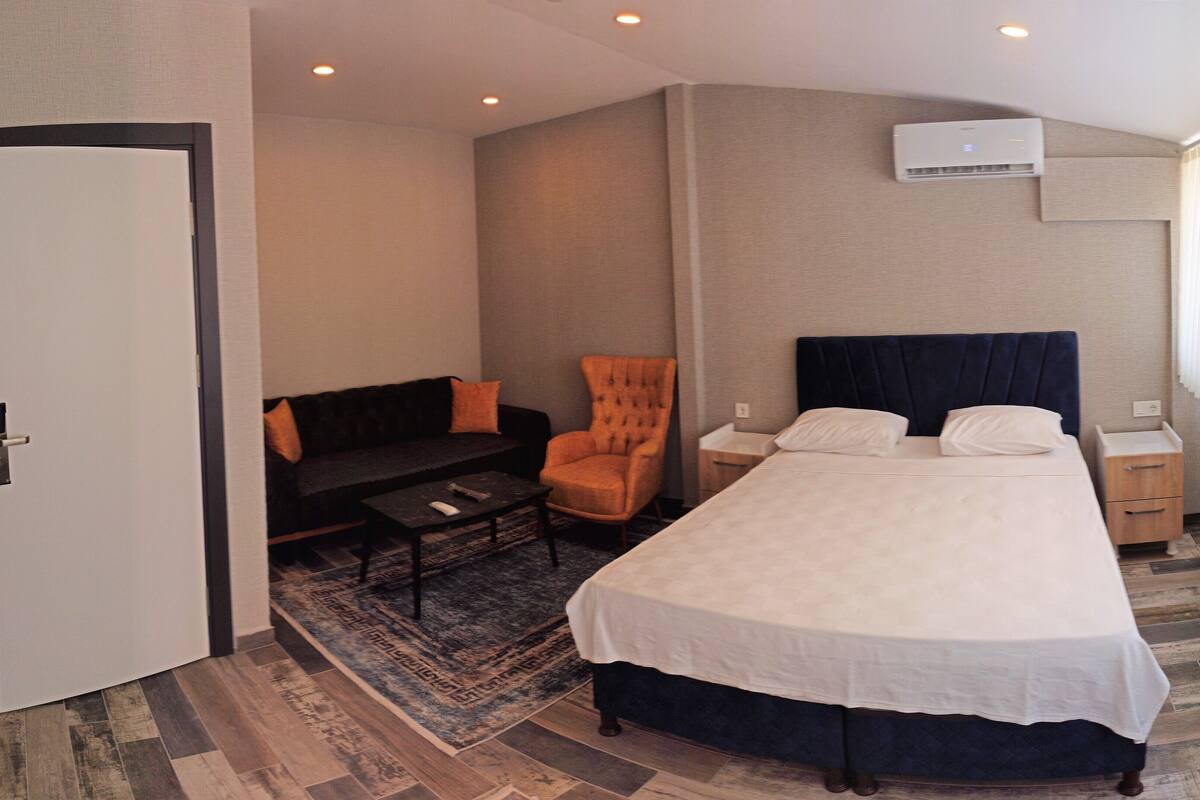A hotel room with a bed, a sofa, a chair, a small table, and a window with curtains.