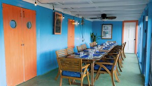 A dining area with a long table set for multiple people, wooden chairs, and a ceiling fan. - Andros Beach Club (Rolle Town)