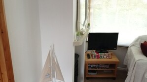 Quarto com uma cama, escrivaninha com computador, estante e janela com persianas.