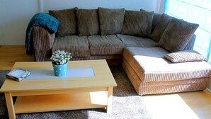 Uma sala de estar com uma mesa de centro de madeira, um vaso azul com bolinhas contendo flores brancas, um sofá listrado marrom e um sofá bege com uma almofada branca.
