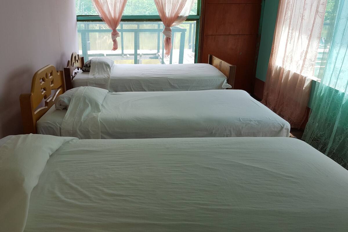 A room with two single beds, a wooden headboard, and a window with sheer curtains.