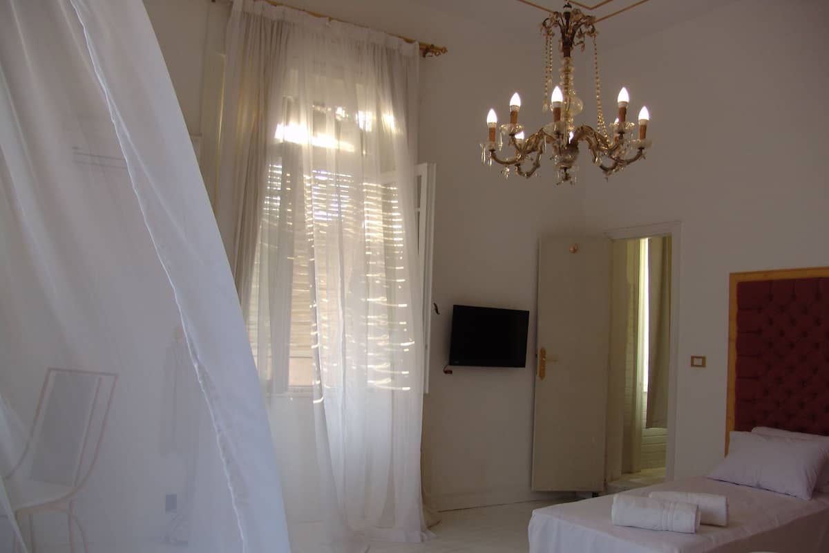 Una habitación de hotel con cama, televisor, candelabro y cortinas translúcidas.