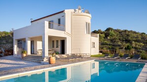 Una casa moderna de dos pisos con piscina, mobiliario exterior y vistas a un paisaje montañoso.