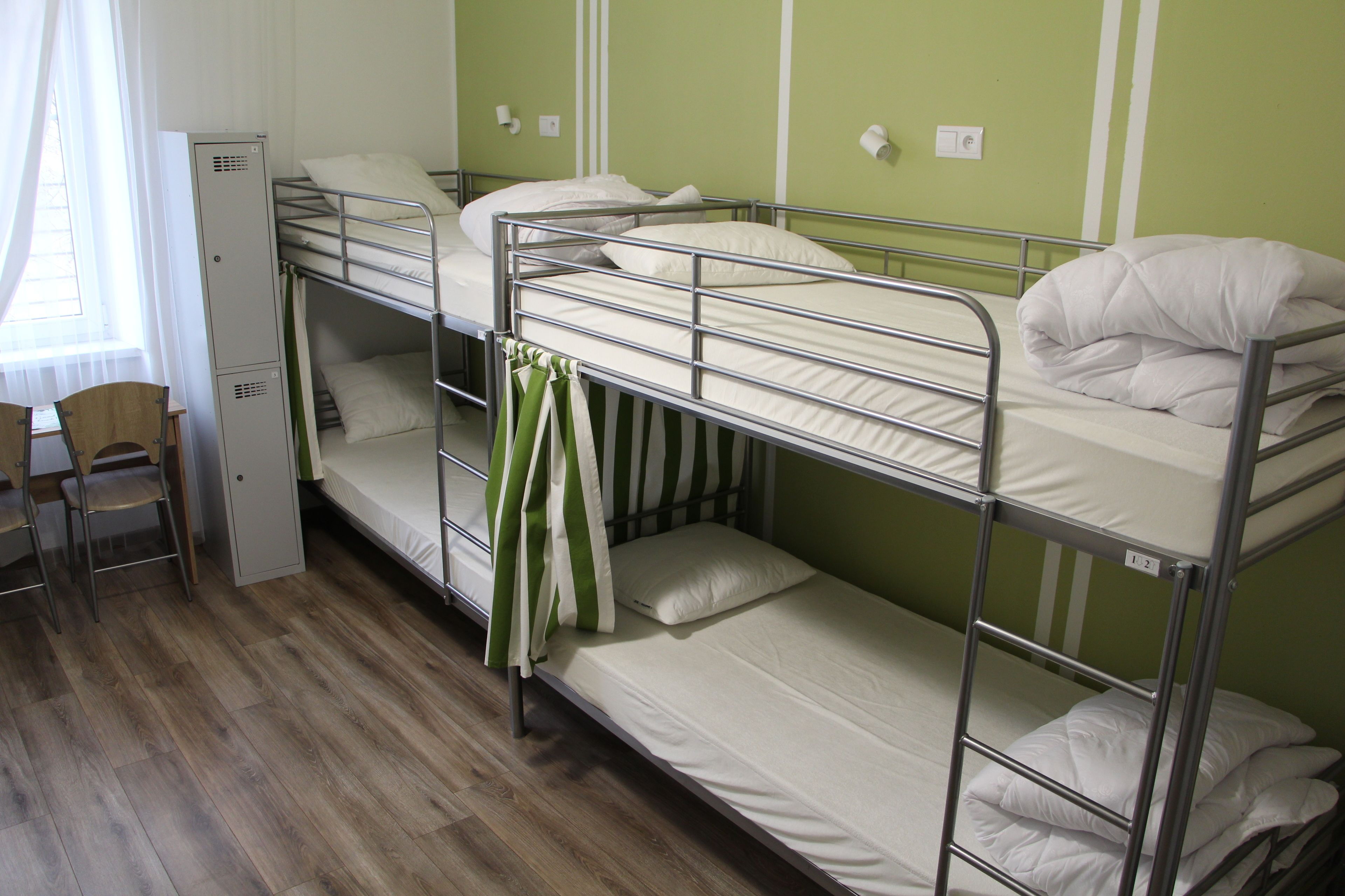 Habitación con literas, un escritorio, una silla, una ventana con cortinas y una pared verde.