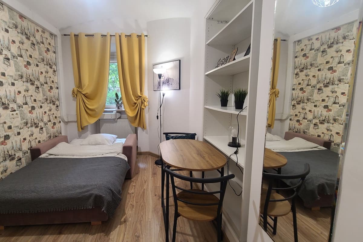 A small, cozy room with two beds, a wooden table, and a mirror.