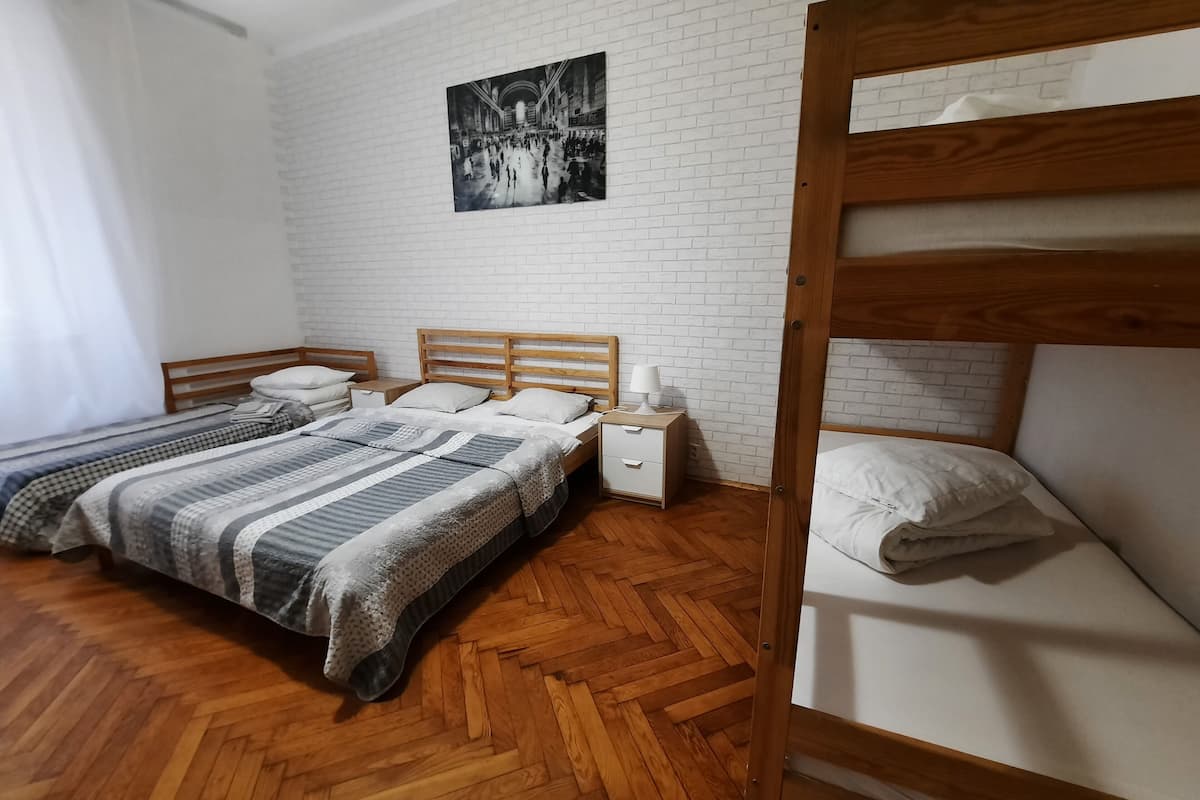 A room with two beds, a wooden floor, a white brick wall, and a black and white photo on the wall.