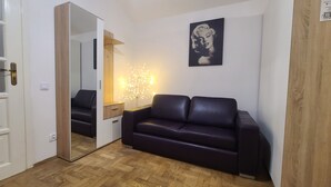 Un soggiorno moderno con un divano in pelle scura, un pavimento in legno, uno specchio, un tavolino con una lampada e un quadro appeso al muro.