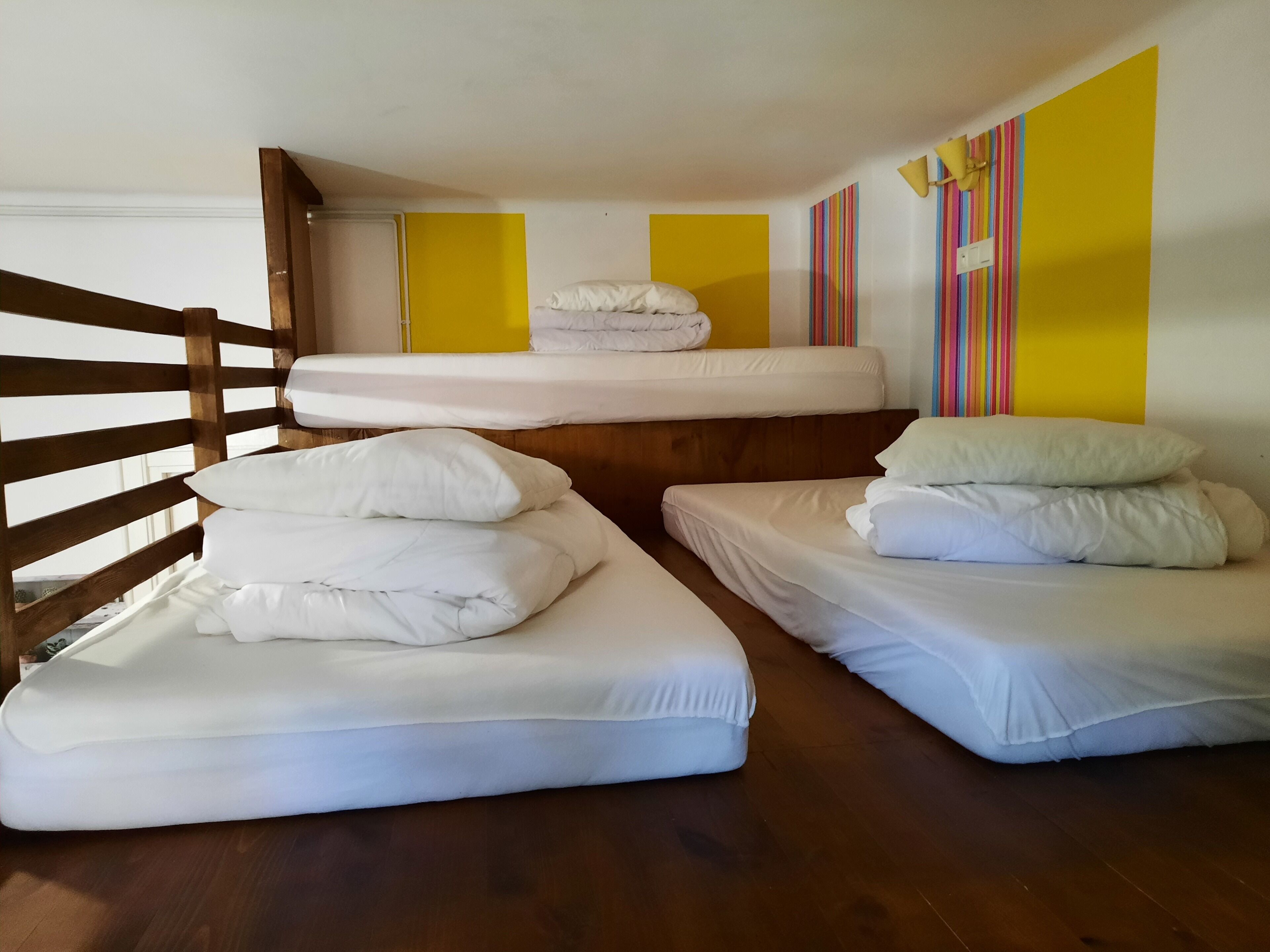 Una habitación con tres literas, cabeceras de madera y una pared de acento amarilla.