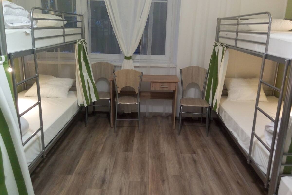 A room with bunk beds, a desk, two chairs, and a window with curtains.