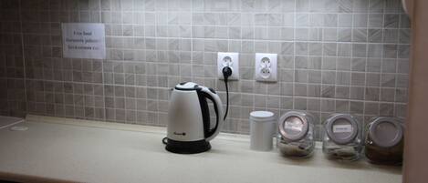 Una cocina con hervidor, cafetera y frascos en la encimera.