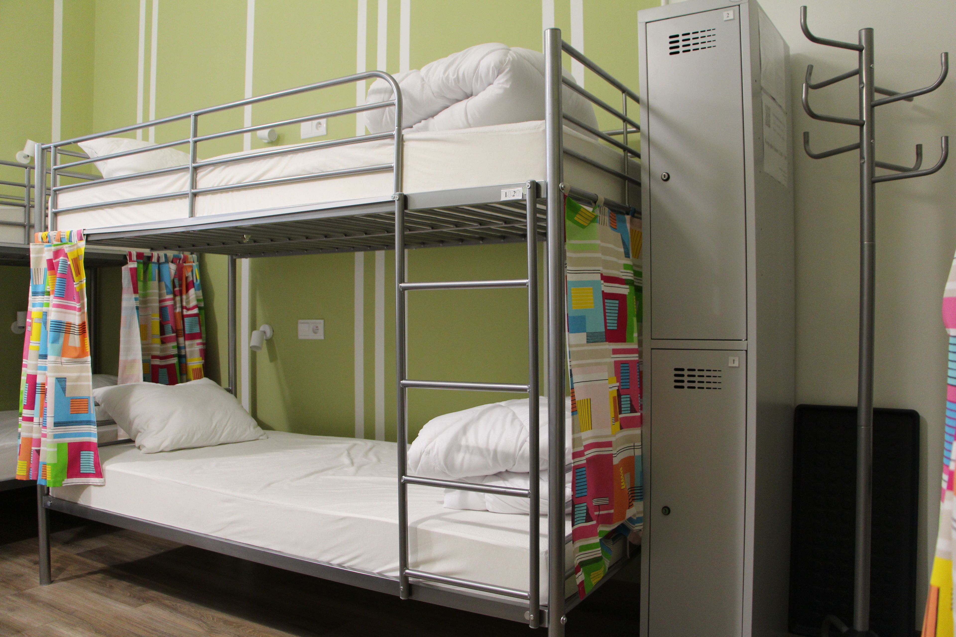 A bunk bed with white bedding, a metal ladder, and colorful curtains.