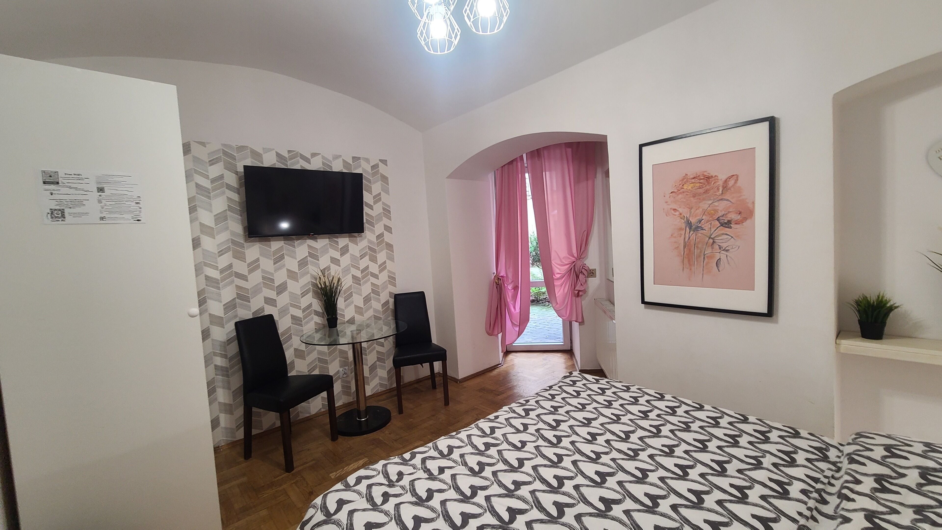 Een slaapkamer met een bed, een televisie, twee stoelen, een kleine tafel en een kamerplant.