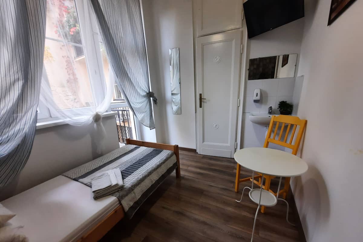 A small room with a bed, a table, a chair, a door, and a window with curtains.