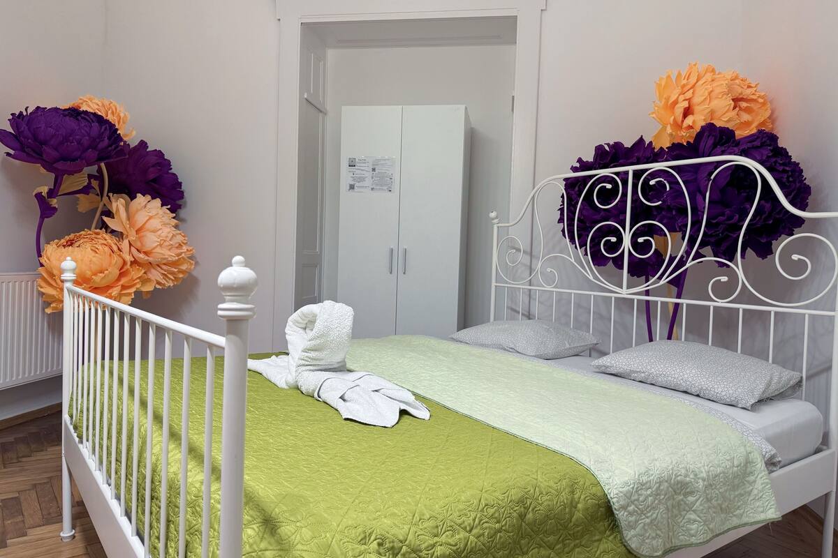 A neatly made bed with a green quilt, white headboard, and two pillows. A white towel is placed on the bed.