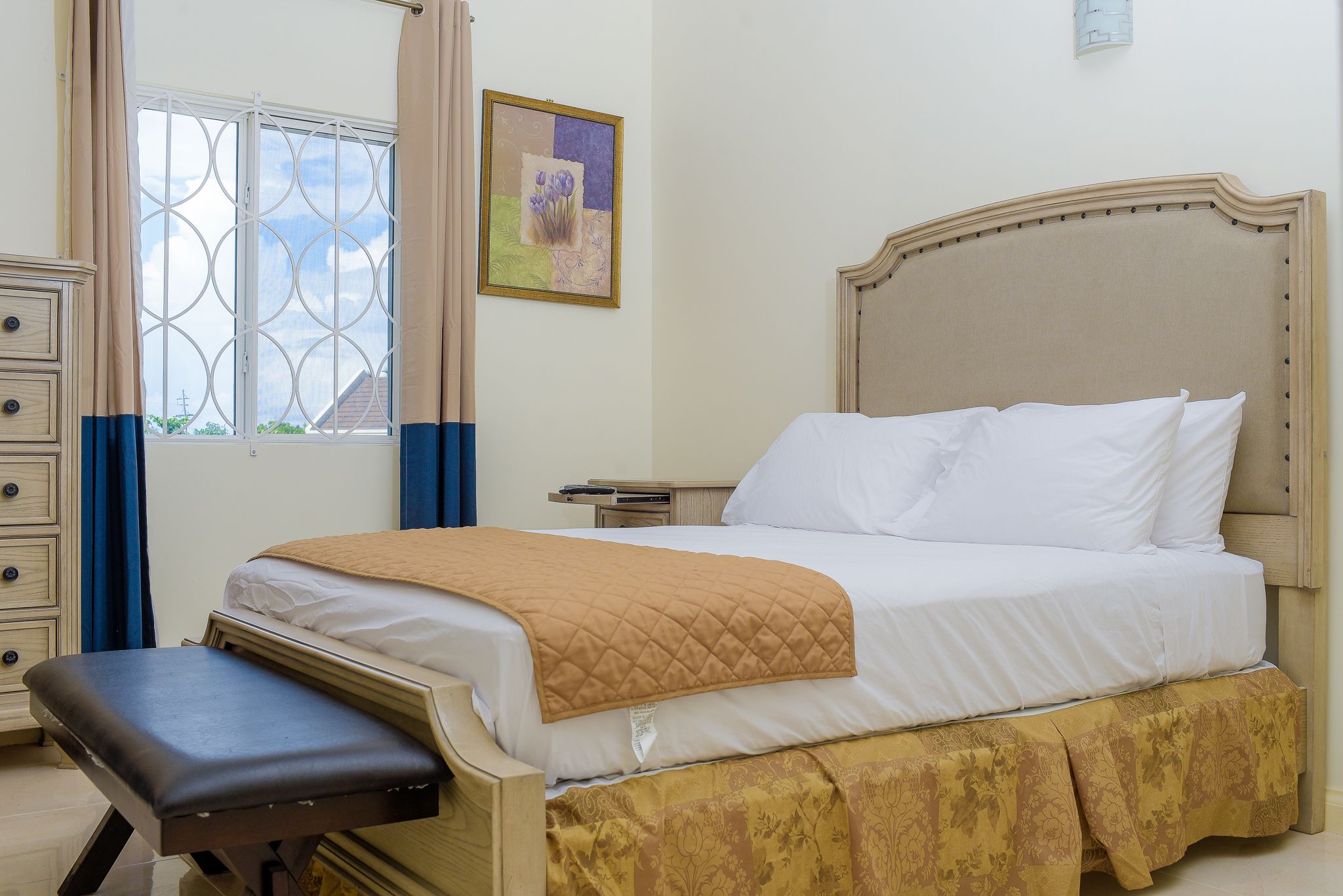 Una camera da letto con un letto, un comodino, una cassettiera, una finestra con tende e un'opera d'arte appesa al muro.