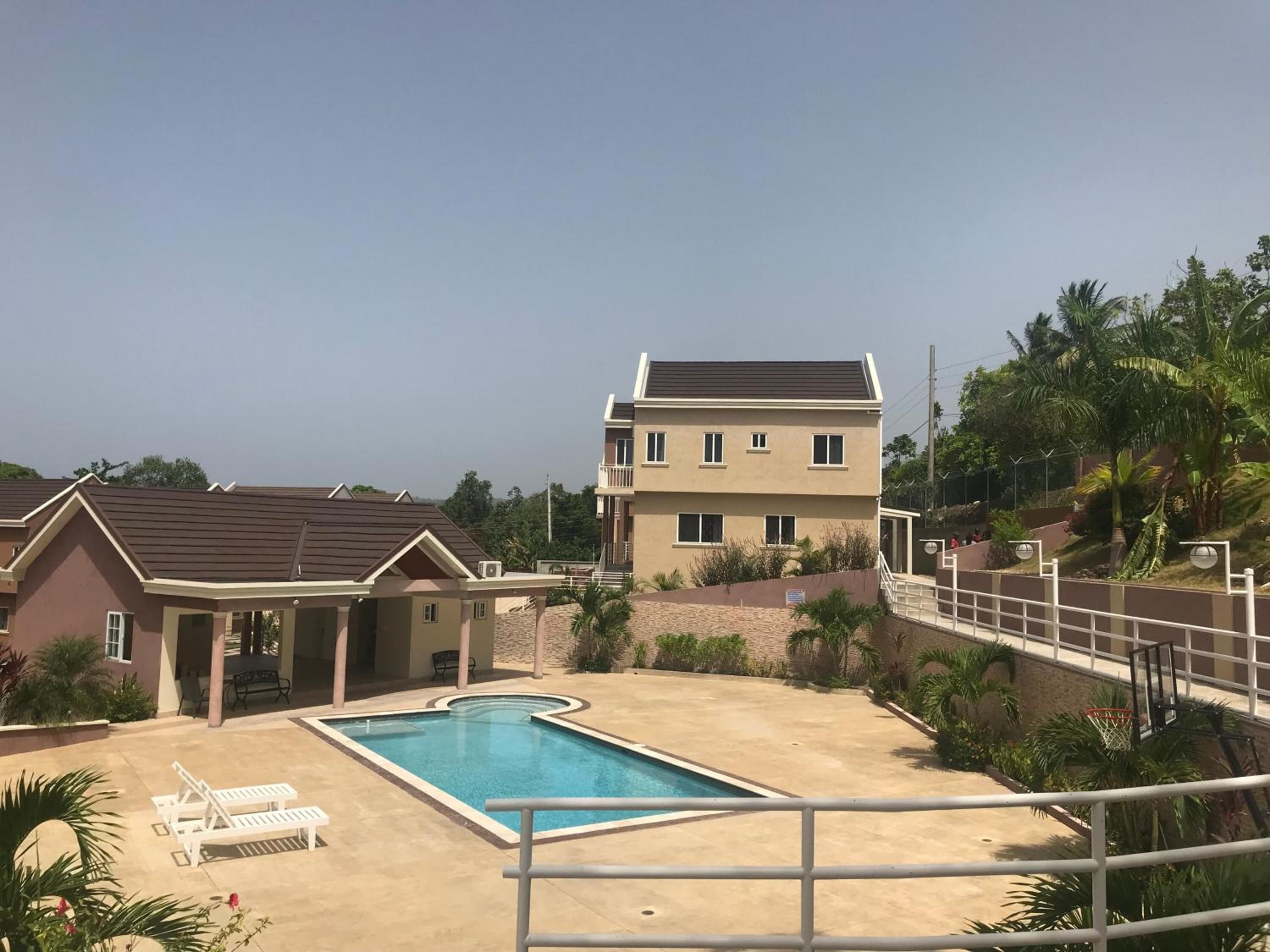 A residential area with a swimming pool, lounge chairs, and a two-story house.