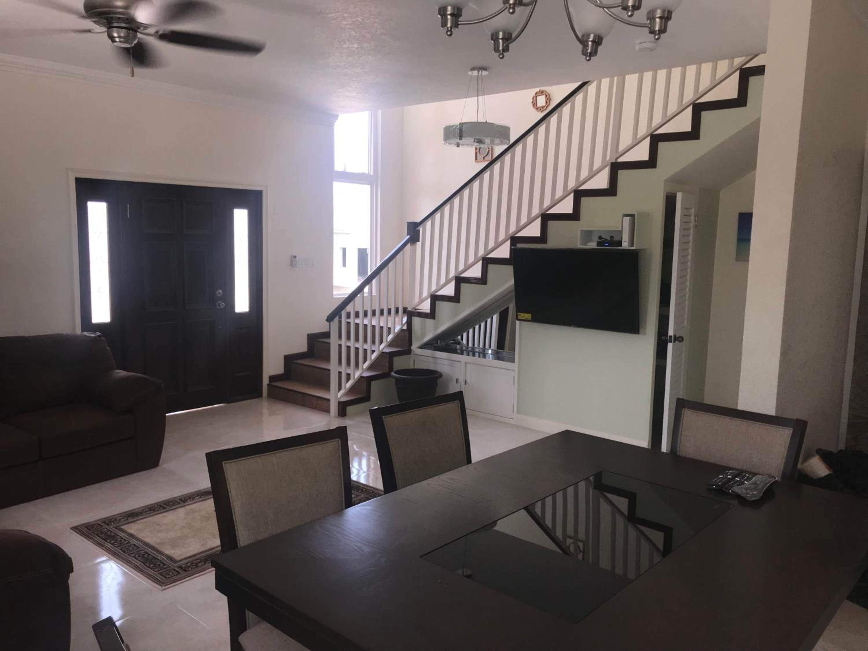 A spacious living room with a dark wooden dining table, a sofa, and a staircase leading to an upper level.
