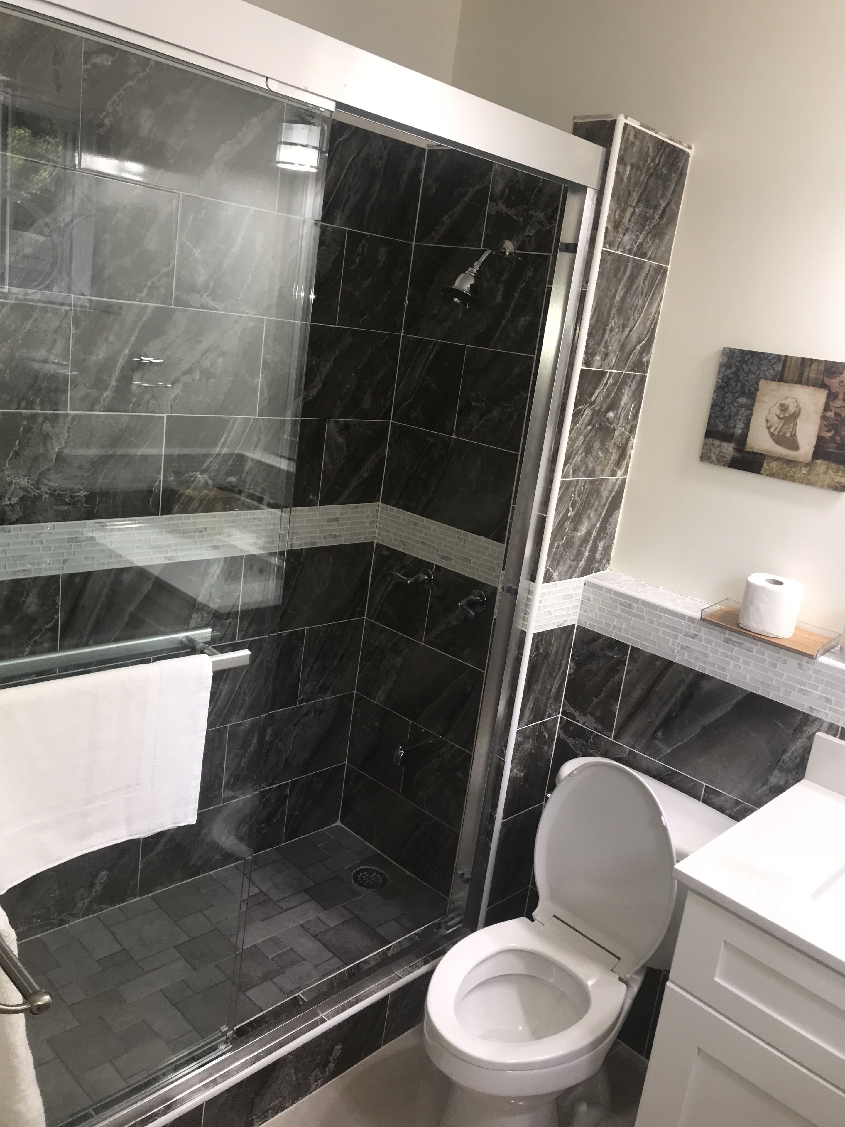 A modern bathroom with a glass-enclosed shower, a white toilet, and a marble-tiled shower area.