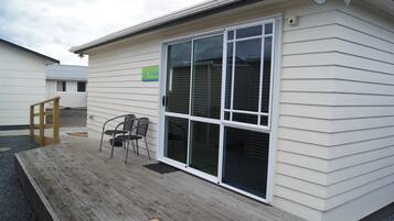 A small building with a sliding glass door, a wooden deck, and two chairs.