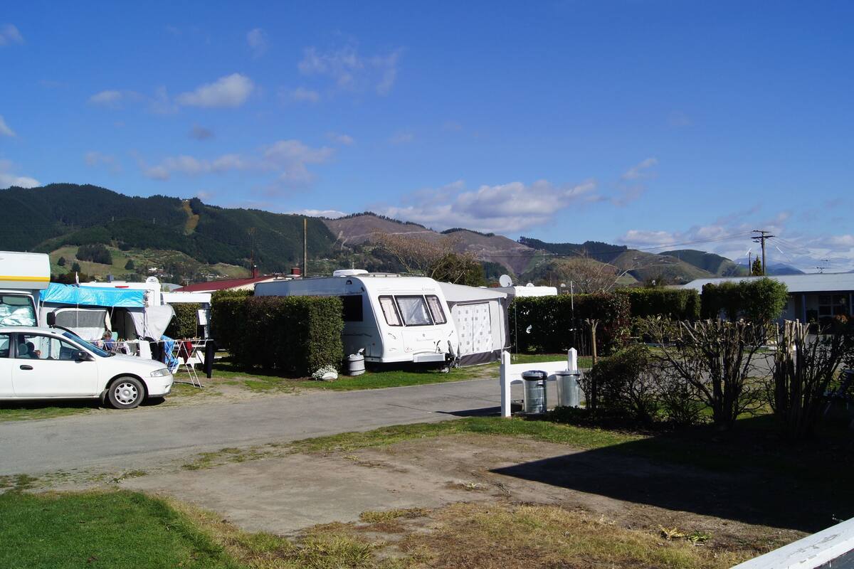 A campsite with RVs and a car parked on a paved area, surrounded by greenery and hills in the background.