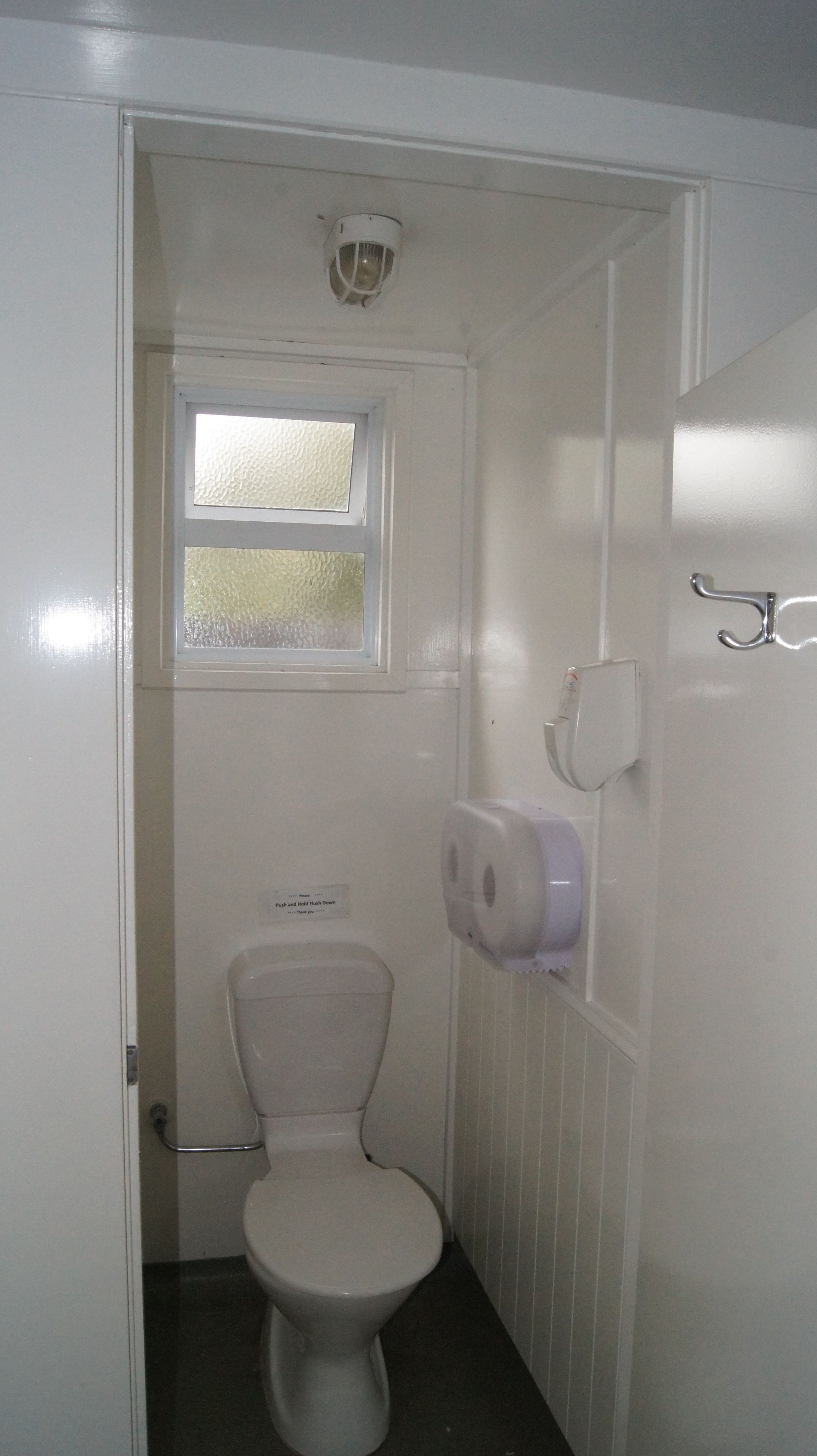 A small, white bathroom with a toilet, a window, and a hand dryer.