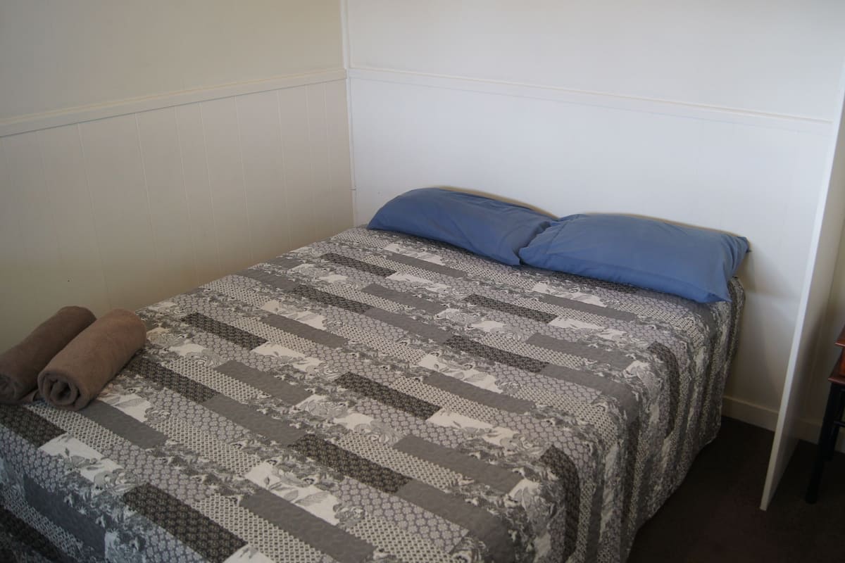 A single bed with a patterned quilt, two pillows, and a wooden nightstand.