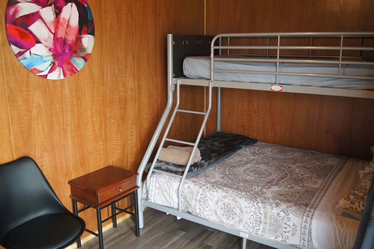 A bunk bed with a ladder, a small wooden table, and a chair in a room with wooden walls.