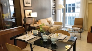 A modern hotel room with a dining area, a sofa, a chair, and a table set for two. - Cozy Pad in Heart of Makati HiSpeed WiFi (Makati)