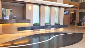 A modern reception area with a marble reception desk, a curved black floor, and a wall-mounted light fixture. - Cozy Pad in Heart of Makati HiSpeed WiFi (Makati)