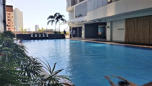 A swimming pool with a stone border, surrounded by greenery and modern buildings. - Cozy Pad in Heart of Makati HiSpeed WiFi (Makati)